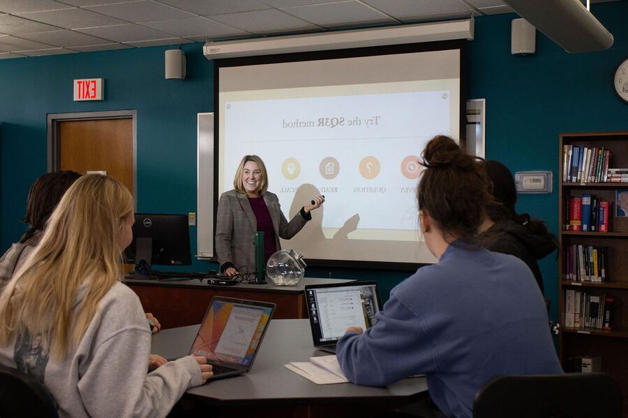 Cooper Center for Academic Excellence director points to a slide projected on a screen in front of students.